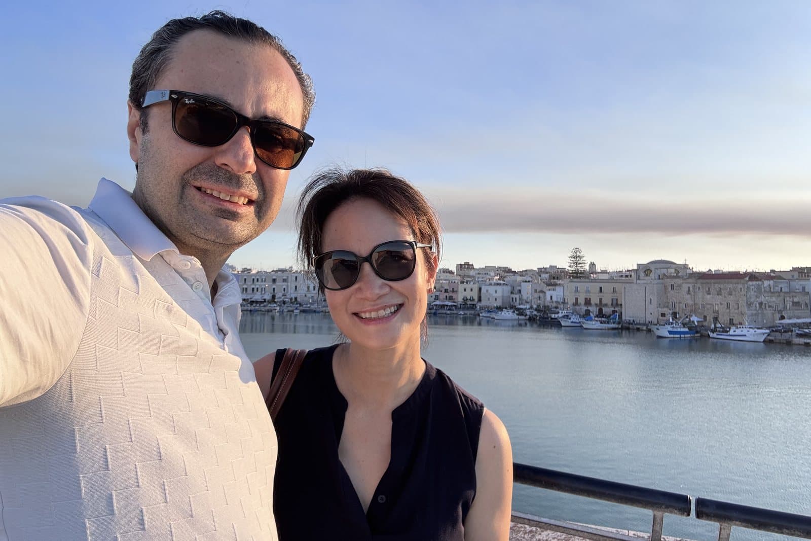 Caitlin and Eugenio on the harbour wall at Trani, late afternoon, with the fishing boats and the low stone town behind them.
