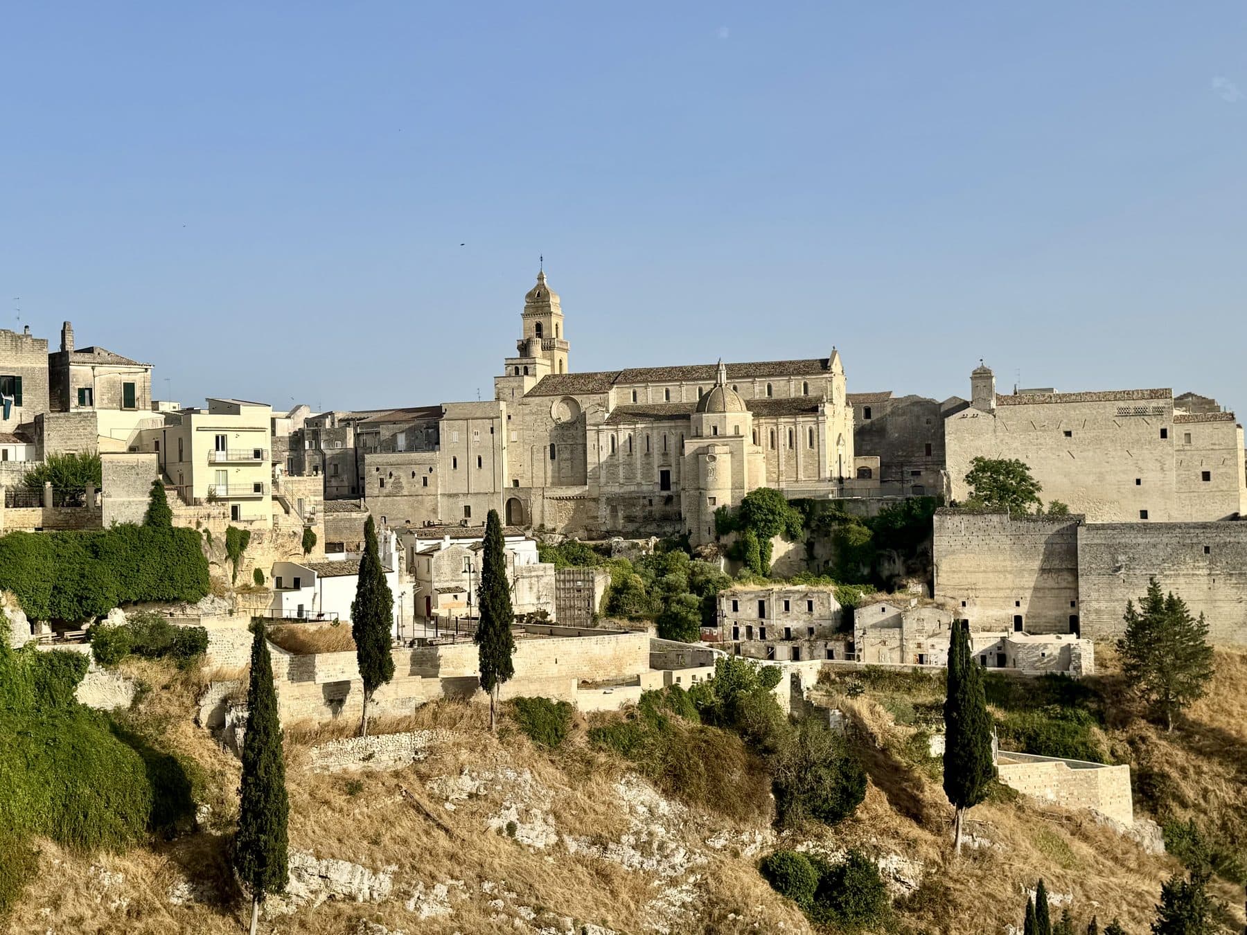 A southern Italian hill town in late afternoon light, its cathedral and stone houses standing above a ravine.