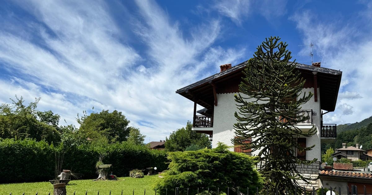 A chalet-style house with a garden and mountain views, behind a wrought-iron fence.