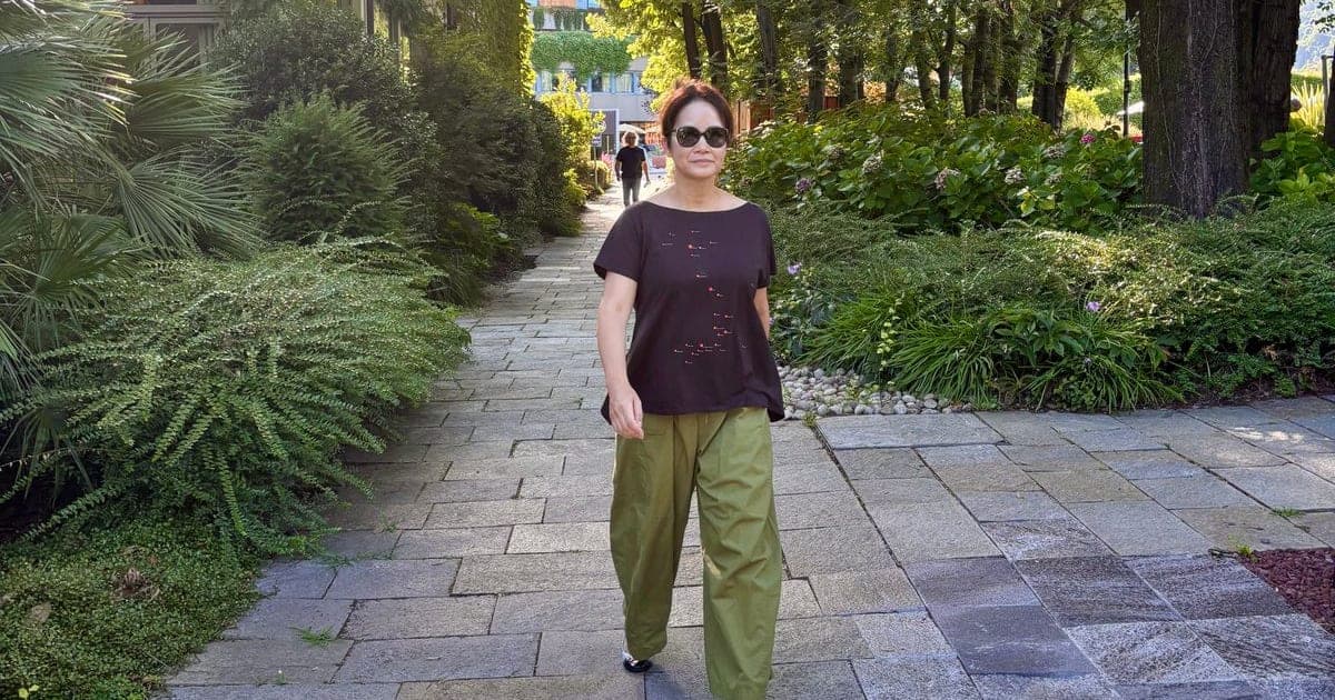 A woman walks along a stone path through a lush green Italian garden.